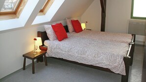 A bedroom with a sloped ceiling, a bed with floral bedding and red pillows, a bedside table with a lamp, and a window with a view.