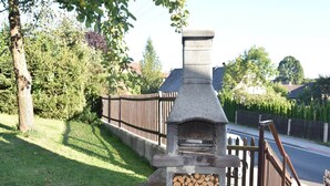 A stone-built outdoor oven with a chimney, surrounded by a wooden fence and a grassy area.