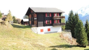 Een chalet met een balkon, gelegen op een helling met een berg op de achtergrond.