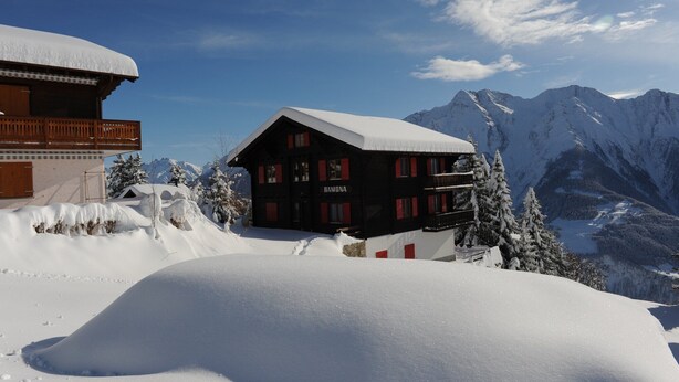Een chalet met een met sneeuw bedekte dak, een balkon en een berg op de achtergrond.