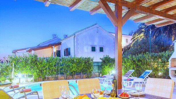 An outdoor dining area with a pool, lounge chairs, and a wooden pergola. - Beautiful villa with spacious terrace and private swimming pool, on the Croatian island of Hvar (Hvar)