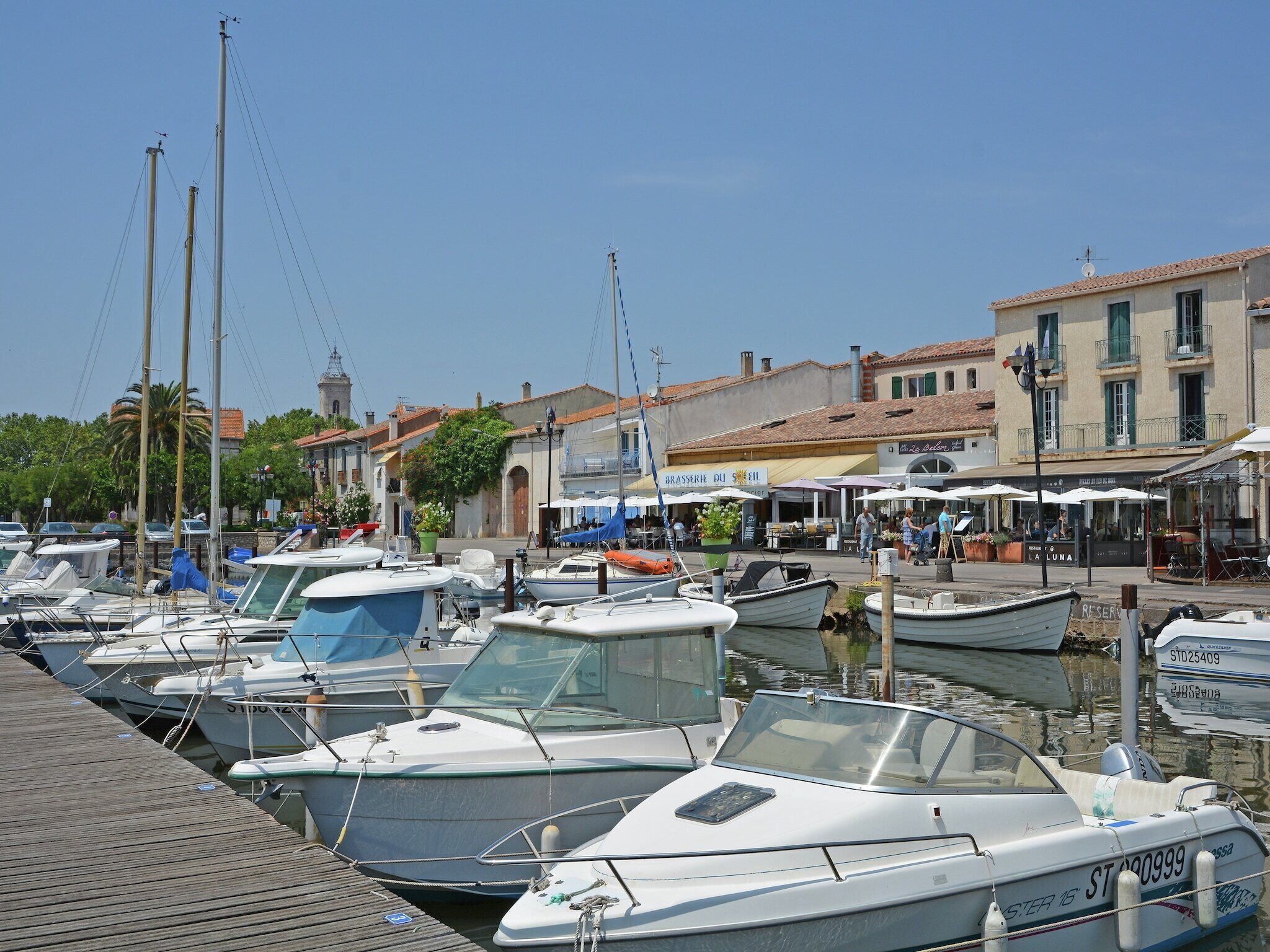A marina with various boats docked, a waterfront restaurant, and buildings with balconies.