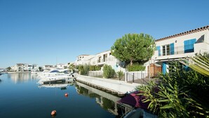 A marina with boats docked, a calm water body, and buildings with blue shutters.