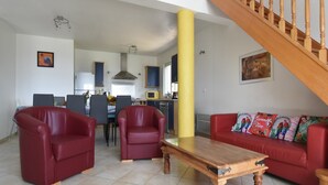 A living room with a wooden staircase, red sofas, and a dining area with chairs and a table. - Courry Views: Pool & Nature (Courry)