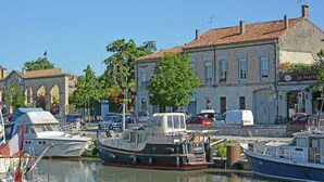 A marina with boats docked, a building with a sign reading "HOTEL", and a clear blue sky. - Courry Views: Pool & Nature (Courry)
