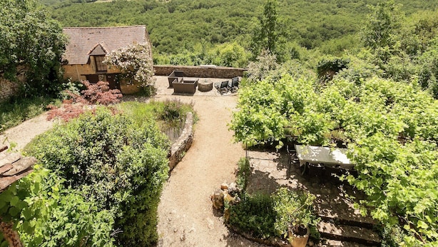 A rustic stone building with a thatched roof, surrounded by lush greenery and a vineyard. - Country House in Dordogne near Lascaux Cave (Les Eyzies-De-Tayac-Sireuil)