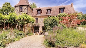 A stone house with a gravel driveway, a garden with various plants, and a clear sky. - Country House in Dordogne near Lascaux Cave (Les Eyzies-De-Tayac-Sireuil)