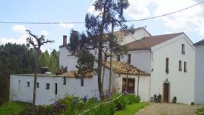 Un bâtiment blanc avec un toit recouvert de tuiles, un chemin de gravier et des fleurs violettes au premier plan.