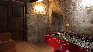 Une pièce avec un mur en pierre, des poutres en bois au plafond et une table de baby-foot rouge.
