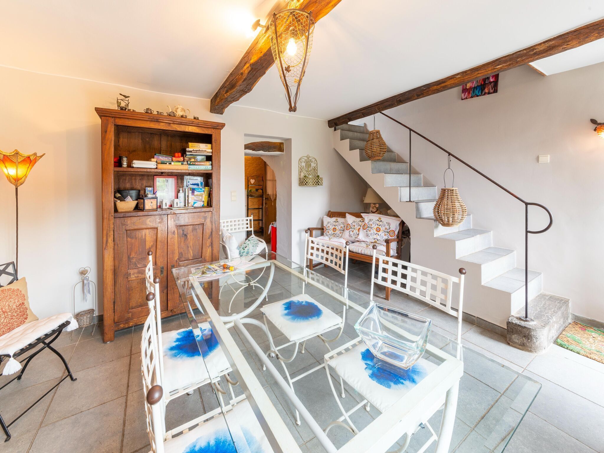 A cozy living room with a glass-top dining table, a wooden cabinet, and a staircase.