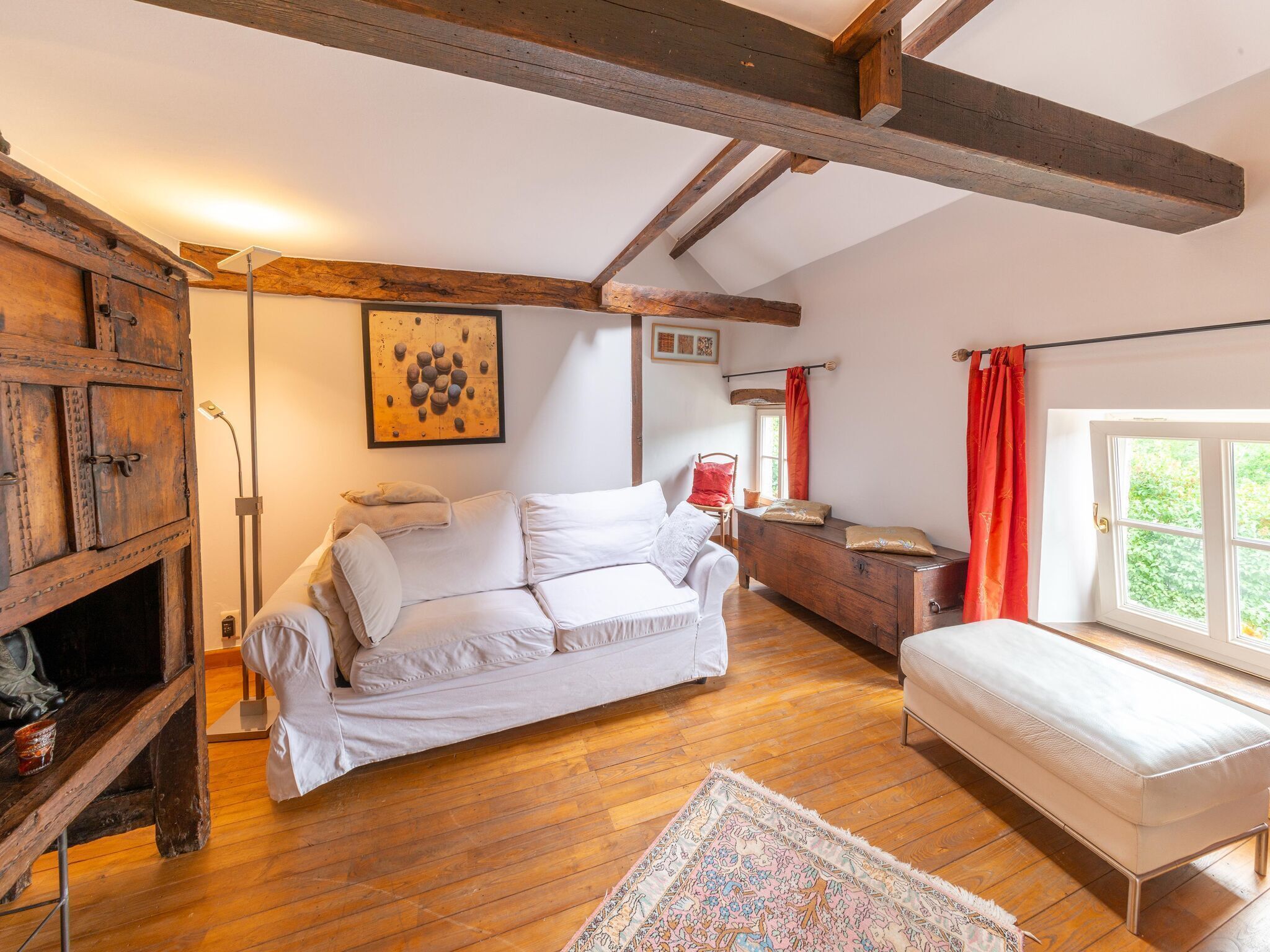 A cozy room with a wooden floor, a white sofa, a small bench, and a wooden cabinet.