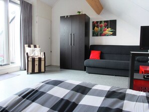 A bedroom with a bed, a sofa, a wardrobe, and a painting of tulips on the wall.