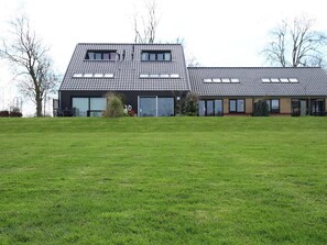 A modern two-story building with a flat roof, large windows, and a grassy lawn in front. - Holiday Home in Langweer with Infrared Sauna (Langweer)