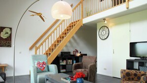 A modern living room with a staircase, a round wall clock, and a flat-screen TV. - Holiday Home in Langweer with Infrared Sauna (Langweer)