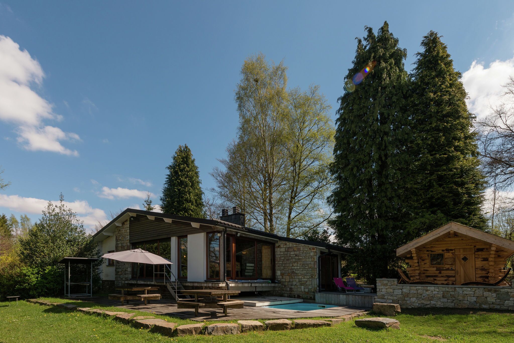 A cabin with a stone exterior, a wooden deck, and a swimming pool.
