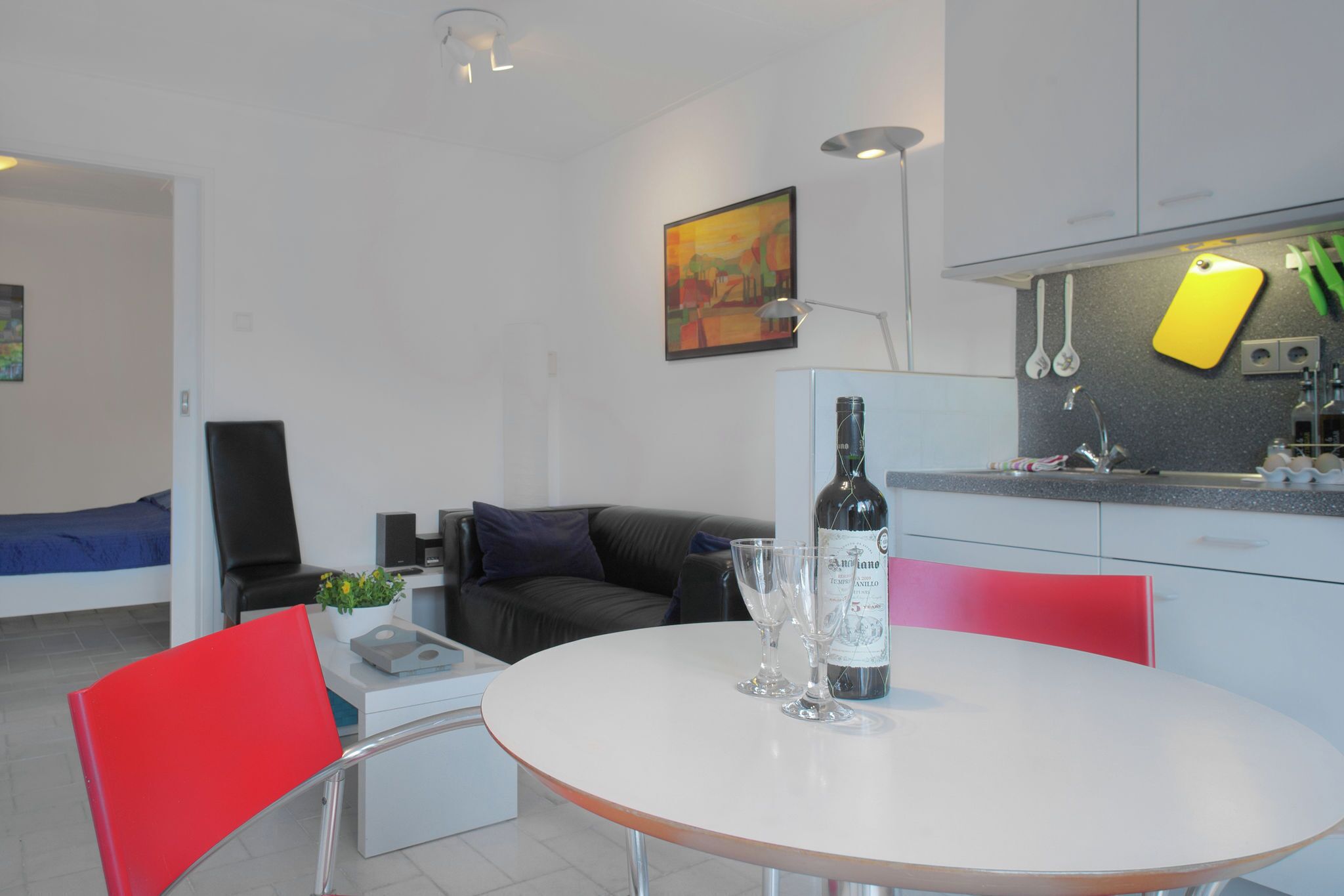 A modern kitchen with white cabinets, a dining table with two chairs, and a bottle of wine on the table.