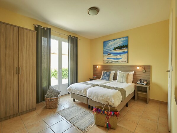 A bedroom with a bed, a nightstand, a lamp, a painting, and a window with curtains.