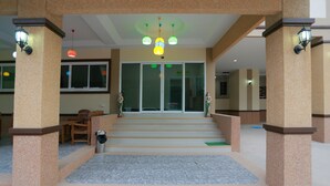 A hotel entrance with a tiled floor, a staircase leading to the entrance, and a reception area with a chair and a trash bin. - V Residence (Nakhon Ratchasima)