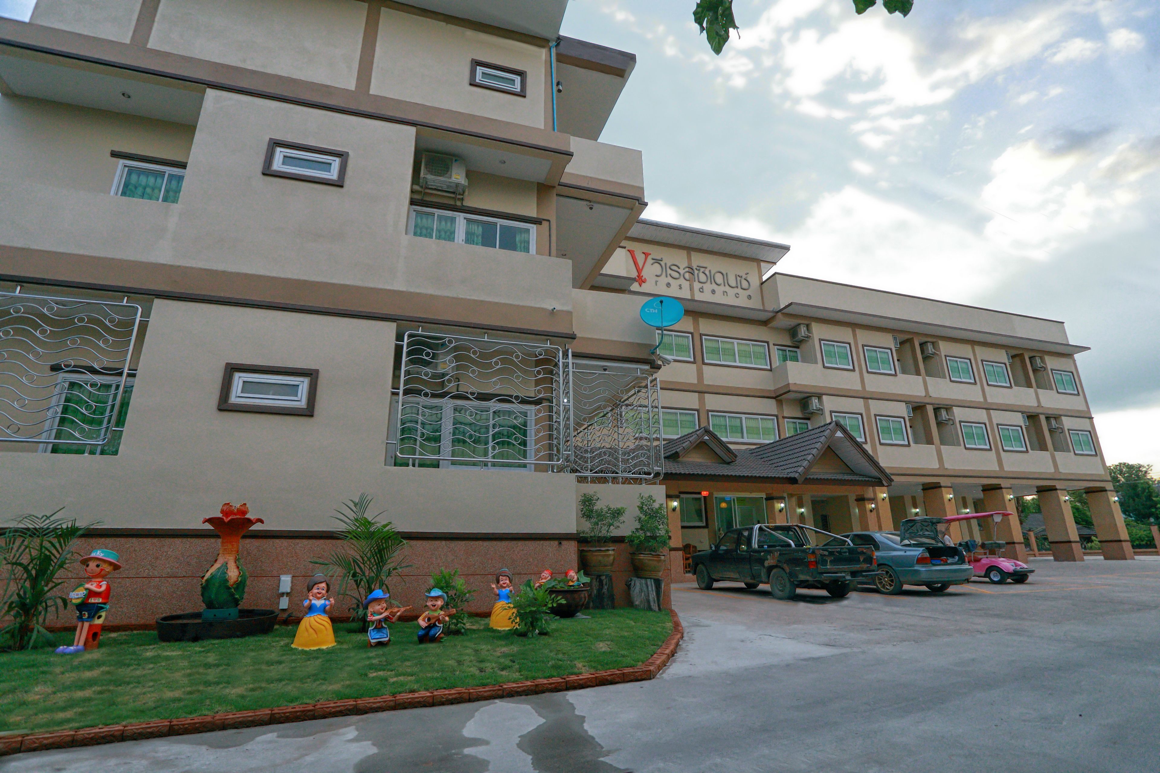 Un hotel de diseño moderno, con varios balcones y un estacionamiento con varios vehículos.
