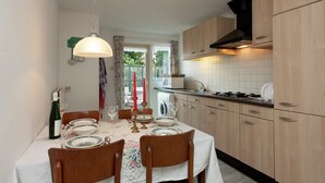 Un coin repas avec une table dressée pour quatre personnes, des meubles en bois, un poêle et une fenêtre avec des rideaux.