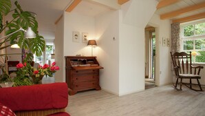 Un salon chaleureux avec un canapé rouge, une commode en bois et un fauteuil à bascule. On y trouve une grande plante aux fleurs rouges et une lampe posée sur la commode.
