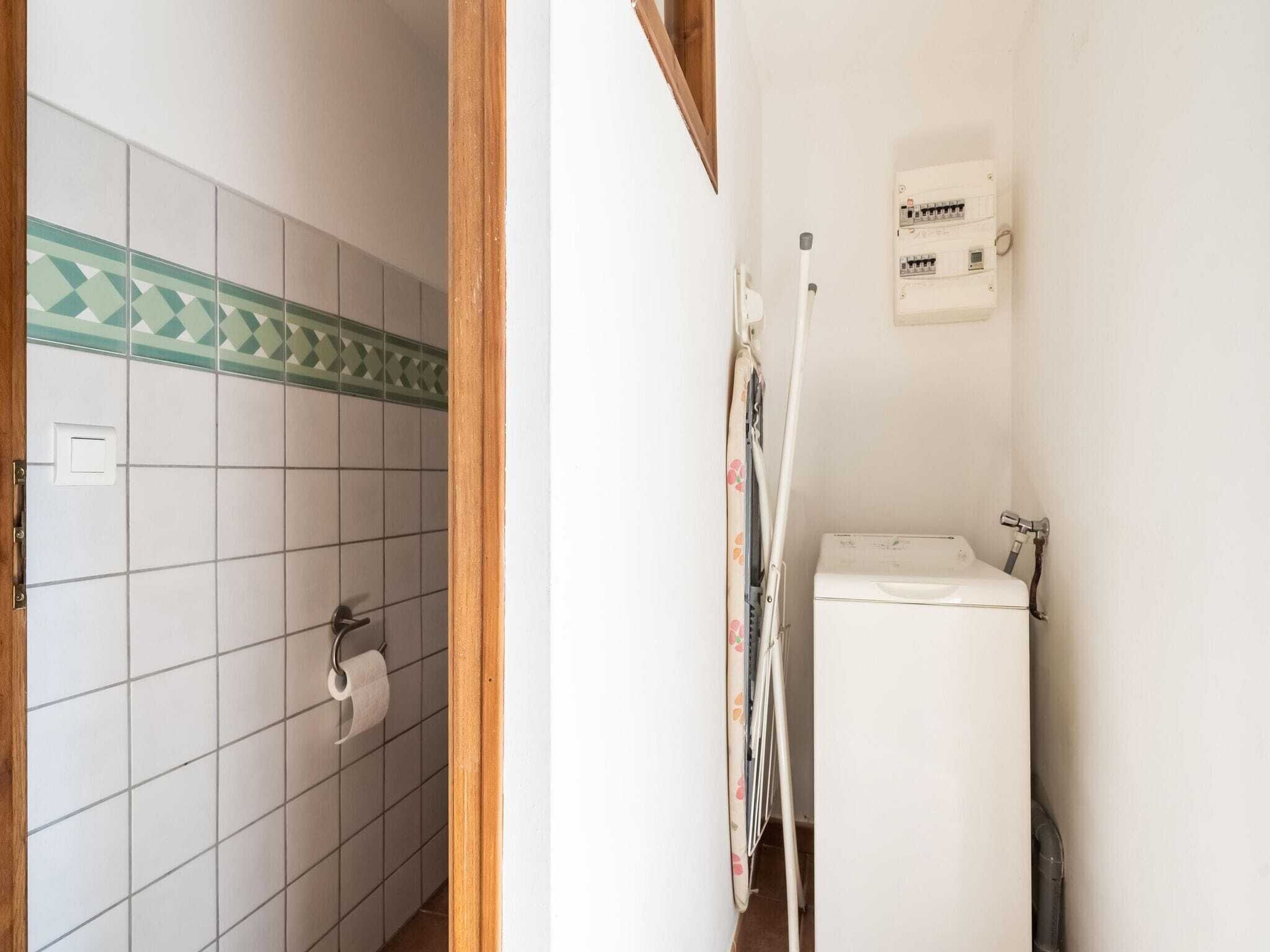 A bathroom with a toilet, a washing machine, and a power outlet on the wall.