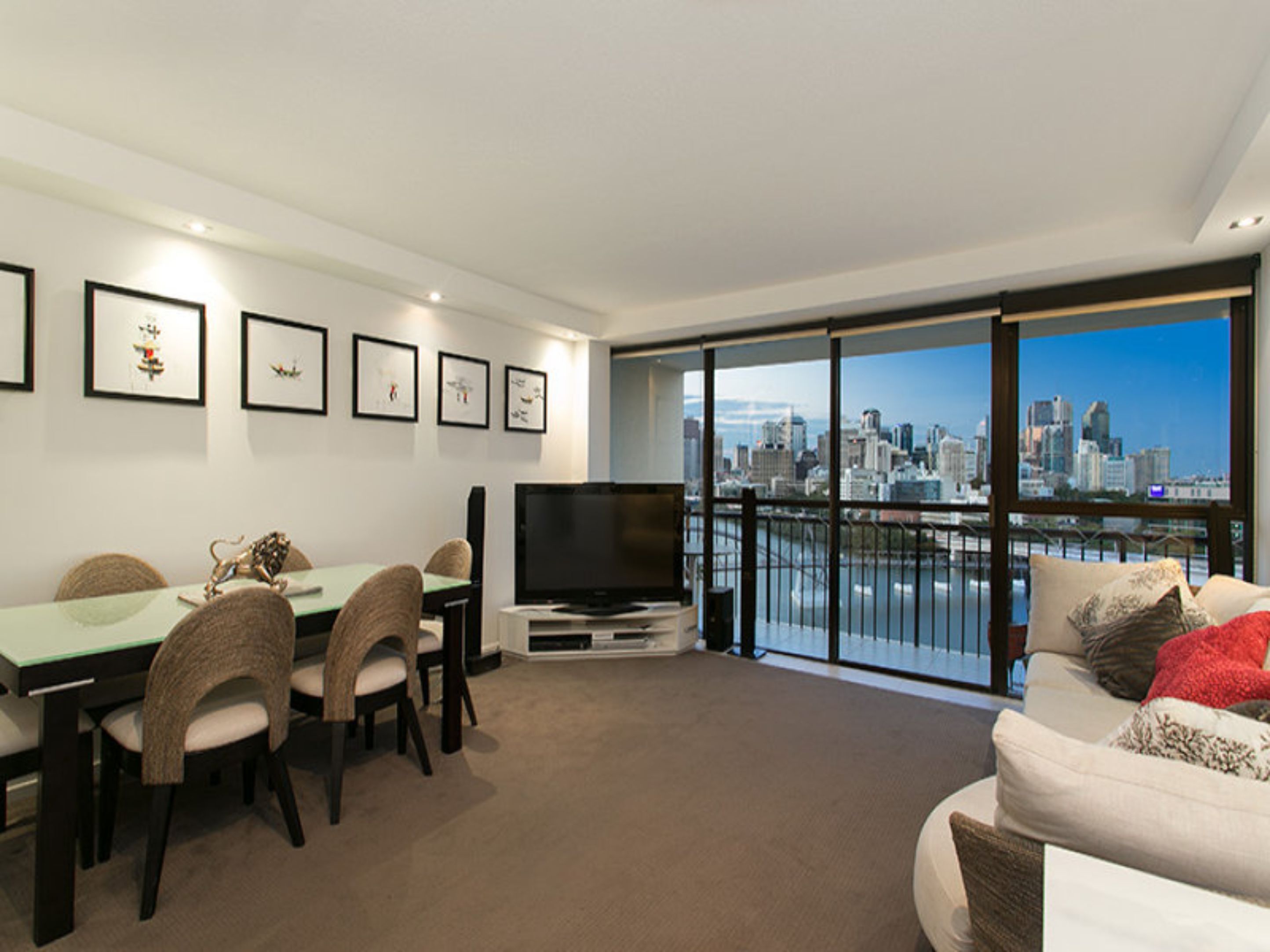A modern living room with a dining area, a flat-screen TV, and a city view through large windows.