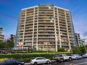 Un hôtel à plusieurs étages, reconnaissable à son grand panneau « River Plaza », doté de balcons et arborant une architecture moderne.