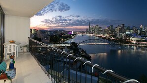 Een balkon met uitzicht op een stadslandschap in de schemering, met een rivier, een brug en moderne gebouwen.