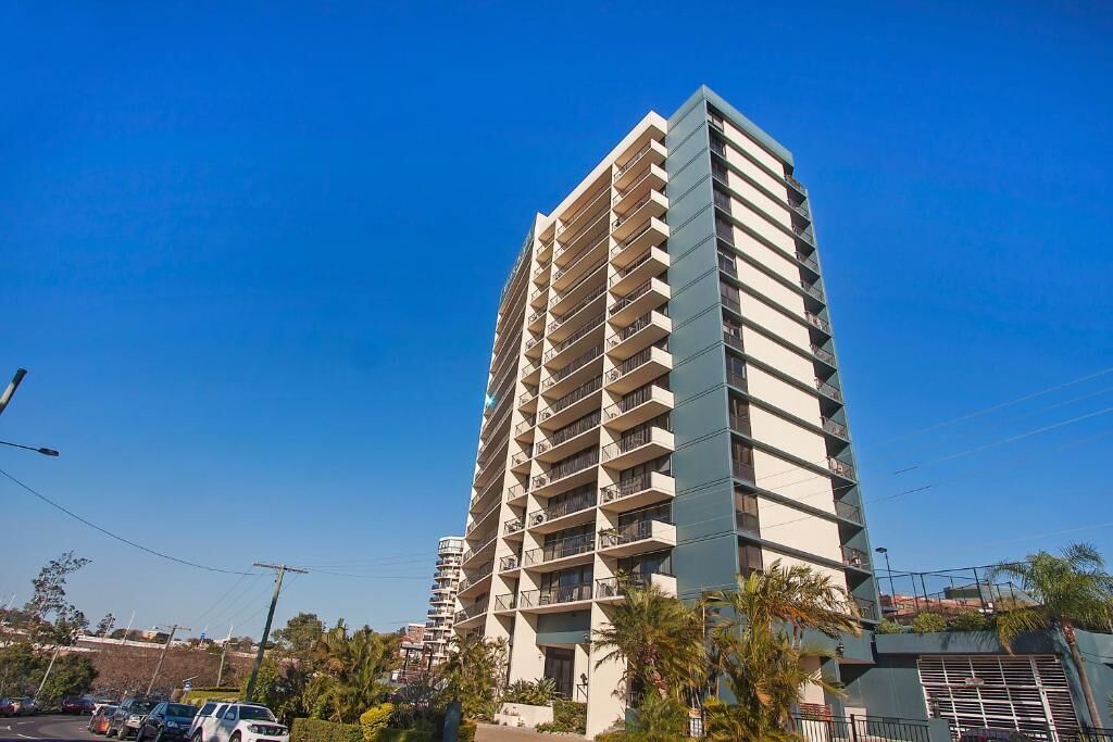 Ein hohes, mehrstöckiges Hotel mit Balkonen an jeder Etage, in der Nähe eines Parkplatzes mit Autos.