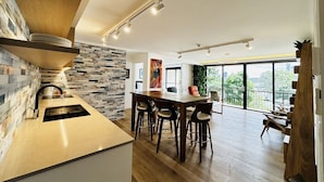 Een moderne keuken met een achterwand van steen, houten vloeren en een eetgedeelte met barkrukken.
