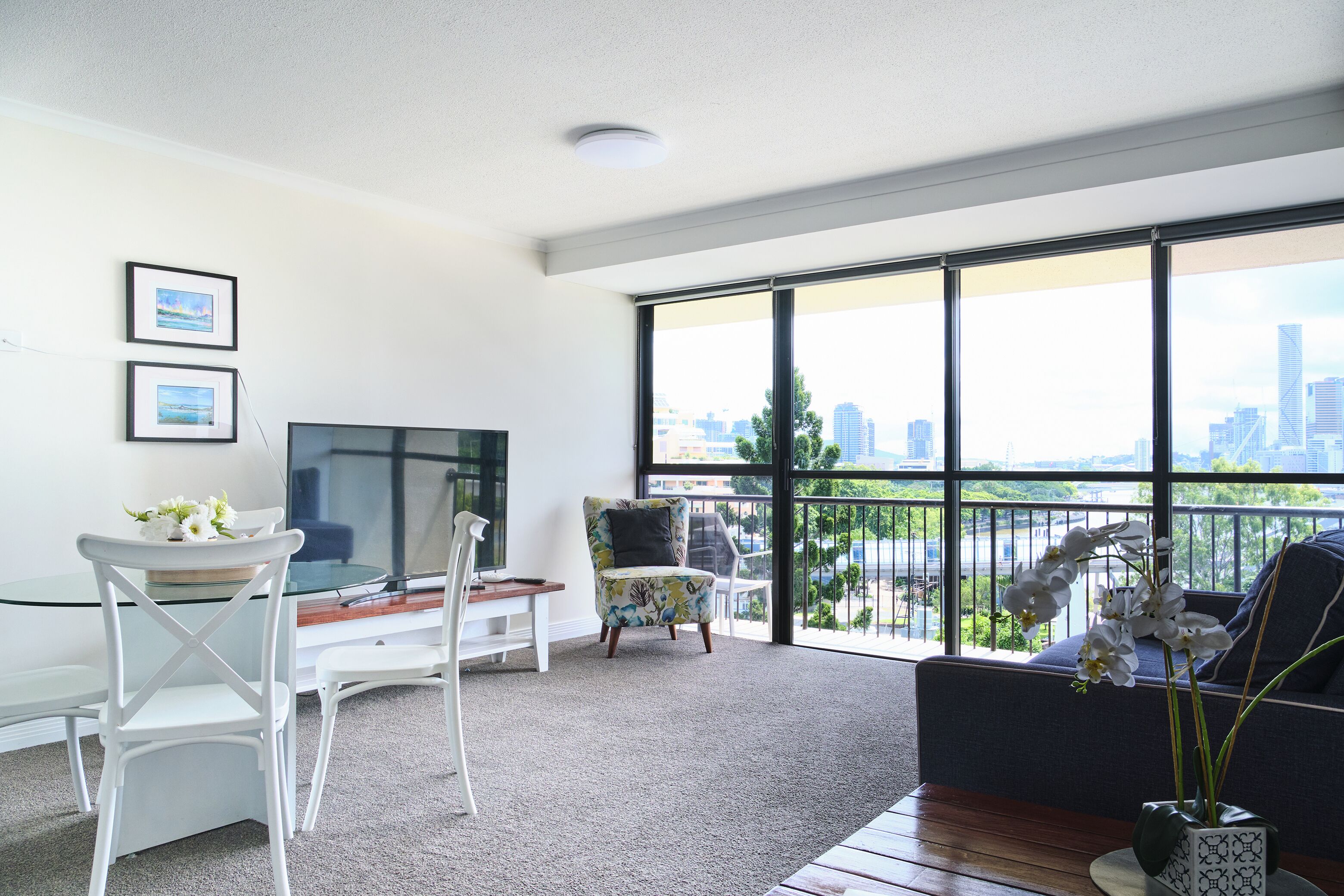 A modern living room with a large window, a flat-screen TV, and a balcony with a city view.