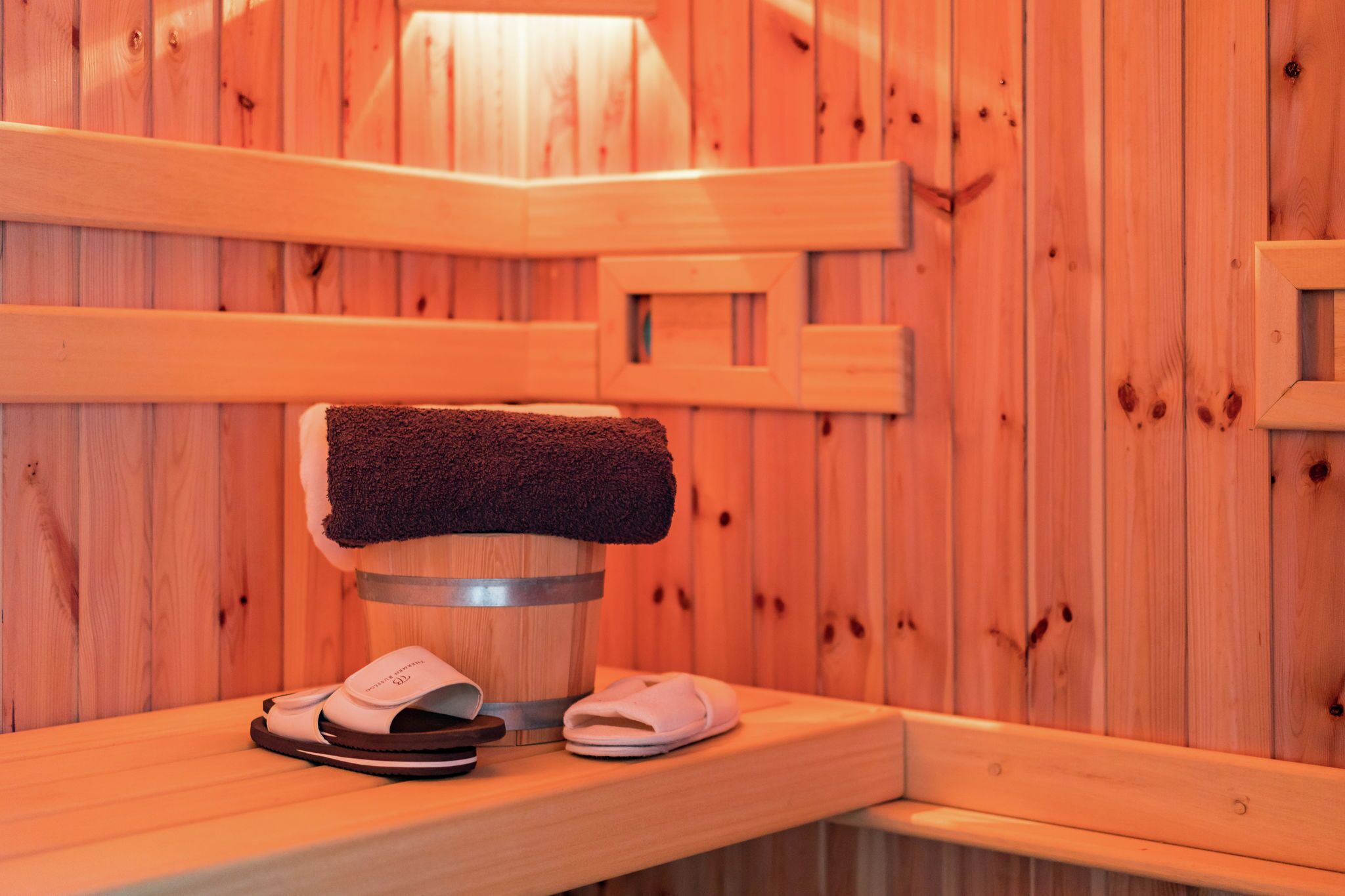 Banco de madera en un sauna, con una toalla y zapatillas.