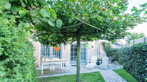 A patio area with a table and chairs, a tree, and a hedge. - Cottage in Ovezande with terrace (Ovezande)