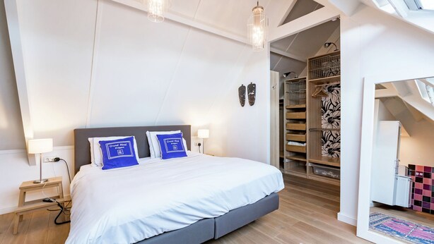 A modern bedroom with a large bed, bedside lamps, a small table, and a walk-in closet with a patterned rug. - Cottage in Ovezande with terrace (Ovezande)