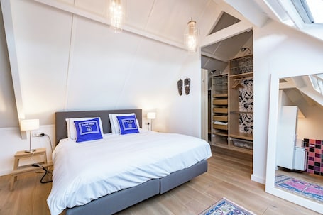 A modern bedroom with a large bed, bedside lamps, a small table, and a walk-in closet with a patterned rug.