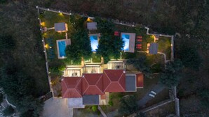 Eine Vogelperspektive auf ein Resort mit mehreren Schwimmbecken, einem Tennisplatz und einem großen Gebäude mit rotem Dach.