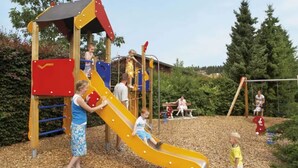 Een speeltuin met een gele glijbaan, klimconstructies en een houten speelhuis.