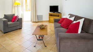 A living room with two sofas, a coffee table, a TV on a wooden stand, and a window with curtains.