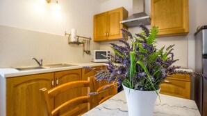 A kitchen with wooden cabinets, a white countertop, a white sink, and a white microwave. There is a white potted plant with purple flowers on the countertop.