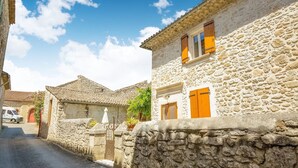 A narrow street lined with stone buildings, featuring a traditional stone wall and a paved road.
