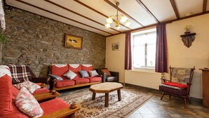 A cozy living room with a stone wall, a wooden ceiling, a red sofa, a wooden coffee table, and a patterned rug.