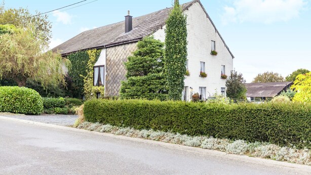 A white house with a sloped roof, surrounded by well-maintained hedges and a clear sky.
