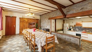 A dining area with a long wooden table and chairs, a stone wall, and a kitchen with modern appliances.