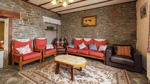 A cozy living room with stone walls, wooden furniture, and a chandelier.