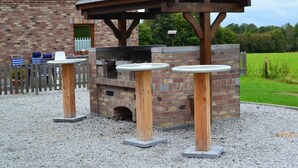An outdoor barbecue area with a brick oven, wooden tables, and a covered seating area.