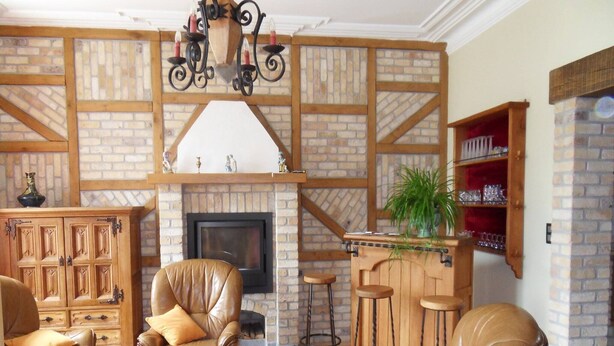A cozy living room with leather sofas, a fireplace, a wooden bar, and a brick wall.