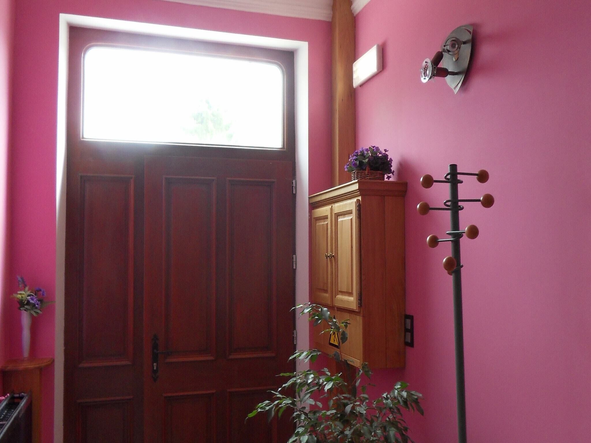 Ein Zimmer mit Holztür, einem kleinen Fenster, einem an der Wand befestigten Kleiderhaken und einem Schrank mit einer Blumenkorb.