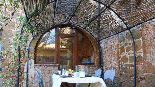 Un espace de restauration extérieur, avec des murs en pierre, comprenant une table dressée pour deux personnes, entourée de chaises en métal.