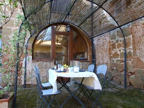 Un espacio al aire libre con paredes de piedra y una mesa preparada para dos, rodeada de sillas de metal.
